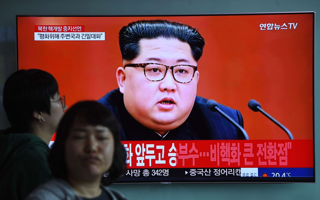 People walk past a television news screen showing a file footage of North Korean leader Kim Jong Un, at a railway station in Seoul on April 21, 2018.