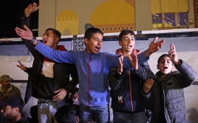 People celebrate while watching a television along a street in Khan Yunis in the southern Gaza Strip on January 15, 2025, amid the ongoing war in the Palestinian territory between Israel and Hamas. Thousands of Gazans celebrated on January 15 as news spread that a ceasefire and hostage release deal had been reached between Israel and Hamas, aimed at ending more than 15 months of war in the Palestinian territory. (Photo by BASHAR TALEB / AFP)