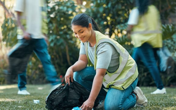 Volunteer helping clean rubbish/trash from park in outdoors grass area.