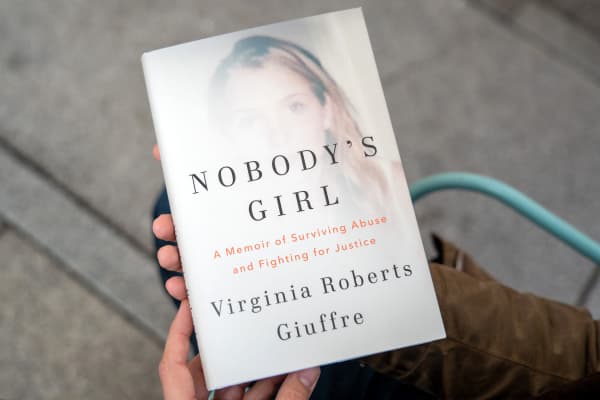 A person poses for a photo with a copy of the book "Nobody's Girl - A Memoir of Surviving Abuse and Fighting for Justice" by Virginia Roberts Giuffre, in central London on October 21, 2025, on the day of its release in the UK. A memoir by one of Jeffrey Epstein's main accusers whose claims led to the downfall of Britain's Prince Andrew was released Tuesday, promising to keep Epstein's ties to President Donald Trump in the spotlight. (Photo by Niklas HALLE'N / AFP)