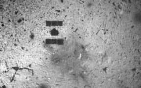 The image taken from on board Japan's Hayabusa-2 spacecraft shows the shadow of Hayabusa2 and a region of the surface that seems to have been discoloured by the touchdown.