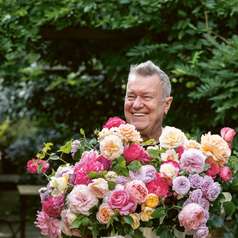 Jimmy Barnes smiles widely and holds a large bunch of beautiful roses.