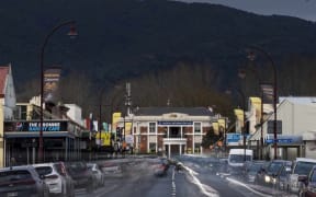 The main street of Paeroa below a grey sky. The photo has long-exposure, showing car headlights moving down the street in a ghostly way.