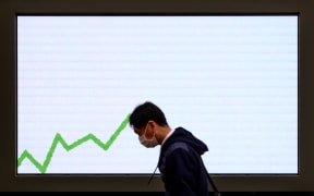 A pedestrian wearing a face mask, amid concerns over the spread of the COVID-19 novel coronavirus, walks past an electronic board displaying an advertisement in Tokyo on February 25, 2020.