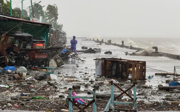 A man stands near debris on a waterfront road amid heavy rain due to weather patterns from Super Typhoon Ragasa in Aparri town, Cagayan province on September 22, 2025. Hundreds of families sheltered in schools and evacuation centres on September 22 as heavy rains and gale-force winds from Super Typhoon Ragasa lashed the northern Philippines and southern Taiwan. (Photo by John Dimain / AFP)
