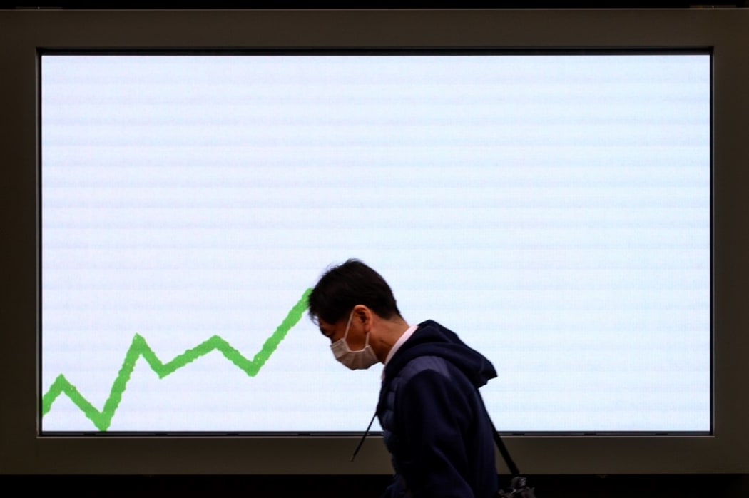 A pedestrian wearing a face mask, amid concerns over the spread of the COVID-19 novel coronavirus, walks past an electronic board displaying an advertisement in Tokyo on February 25, 2020.