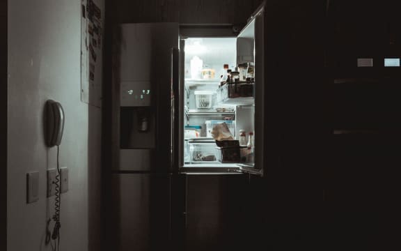 An open fridge door in a darkened room.