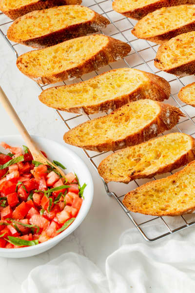 A rack holding toasted crostini slices and a bowl of tomatoes to serve with.