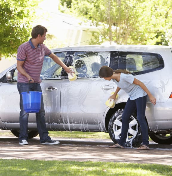 A photo of a father washing his car with histeenage daughter
