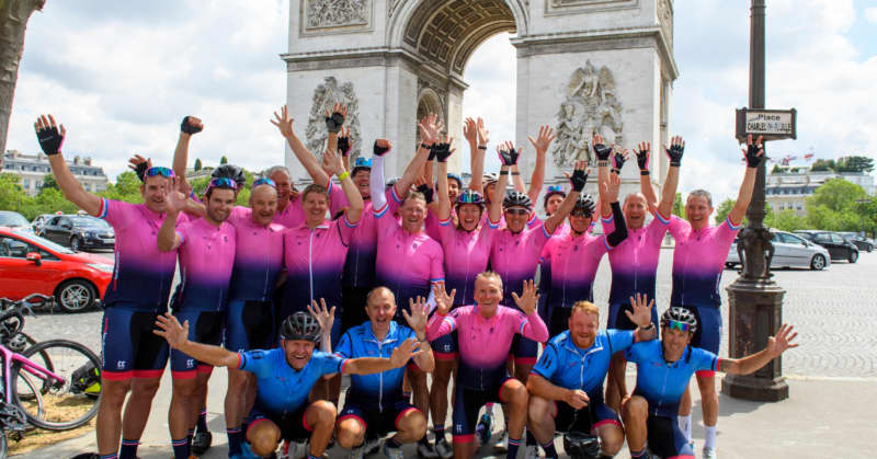 A group of riders of the 2021 Tour 21 raise their hands in the air in front of the Champs-Élysées after completing the Tour de France.