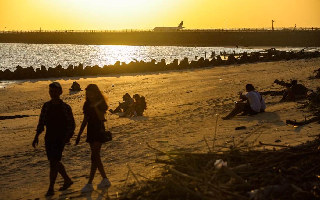 A plane lands at Ngurah Rai international airport as people watch sunset in Kelan Beach, Badung Regency, Bali, Indonesia, on 22 May 2023.