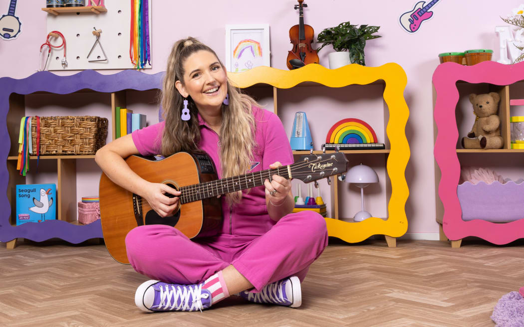 Michal Bush, in all pink, plays a guitar in her music room.