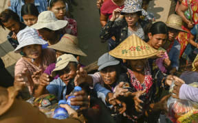People reach up for food aid being distributed in Sagaing on April 3, 2025, following the March 28 earthquake. The shallow 7.7-magnitude earthquake on March 28 flattened buildings across Myanmar, killing more than 3,000 people and making thousands more homeless. (Photo by Sai Aung MAIN / AFP)
