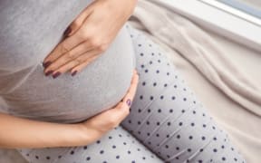 Pregnant woman holding hands on belly indoors
