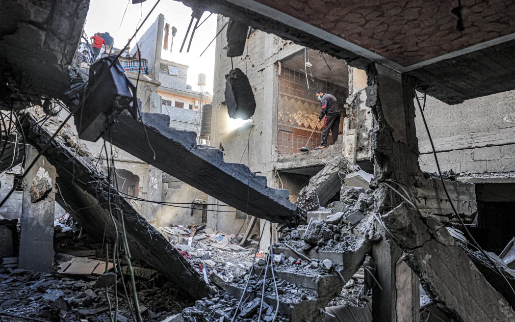 A man sweeps a room with an empty wall overlooking a building destroyed by Israeli bombardment in Rafah in the southern Gaza Strip on December 24, 2023 amid the ongoing conflict between Israel and the militant group Hamas. (Photo by SAID KHATIB / AFP)