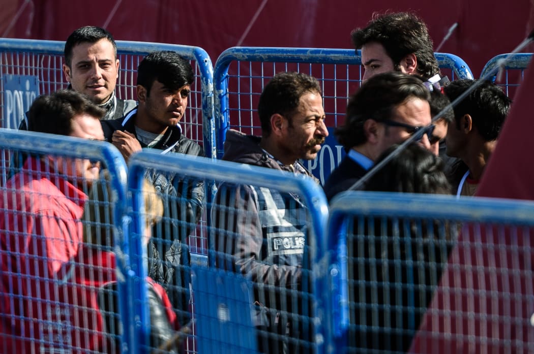 A police officer escorts a deported migrant from a small Turkish ferry carrying migrants who are deported to Turkey on April 4, 2016 as they arrive at the port of Dikili district in Izmir.