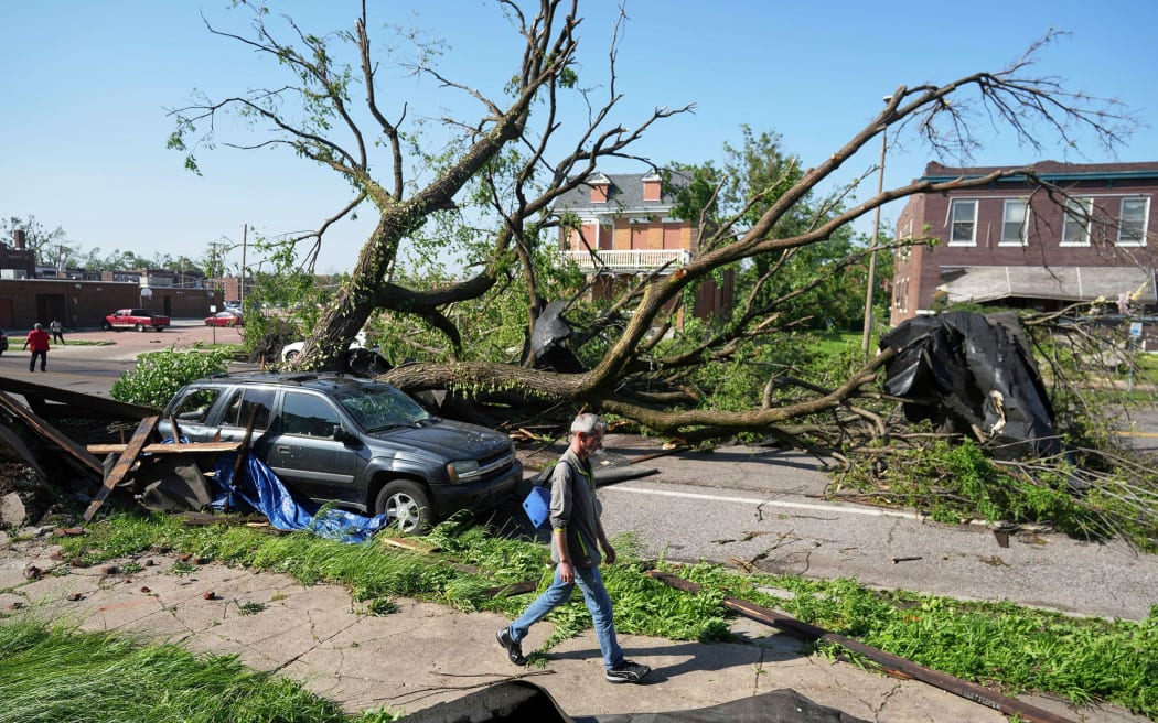 A person walks past a large tree blocking a road after a severe storm moved through in St. Louis, on Friday.