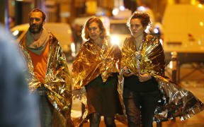People wrapped in life emergency blankets walk near the Bataclan concert hall in central Paris, early on November 14, 2015.