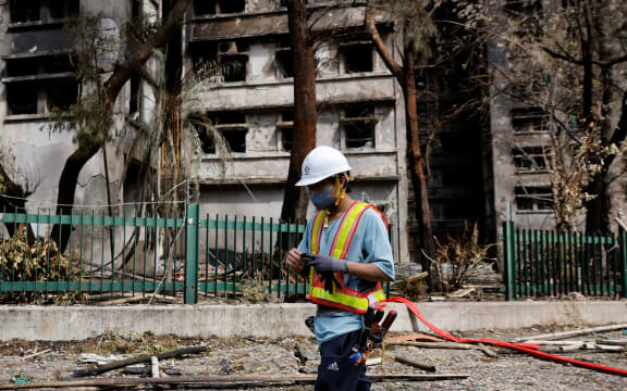 A repair worker walks past burnt buildings after the deadly fire at the Wang Fuk Court housing complex, in Tai Po, Hong Kong, on November 29, 2025.
