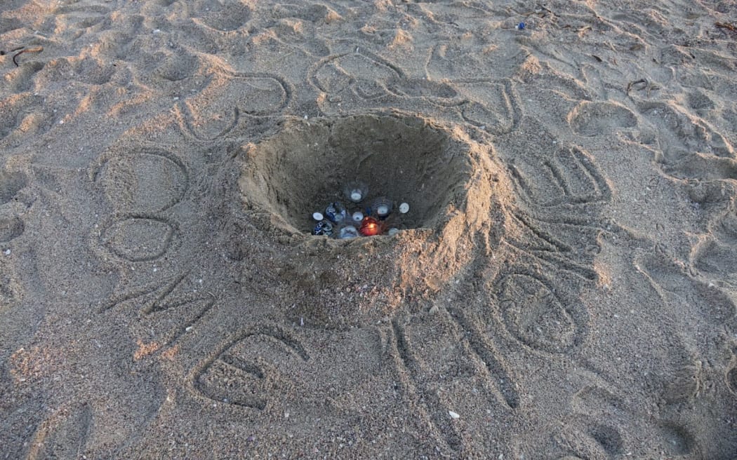 A message reading "Come Home" is left in the sand after a candle-lit vigil.