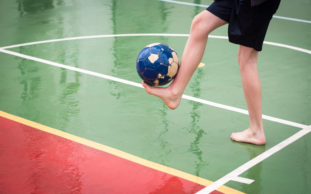 Barefoot boy playing football on a wet sports court.