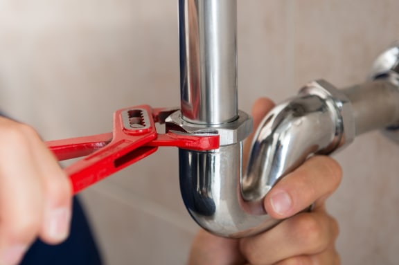 A plumber fixes a pipe with a wrench.