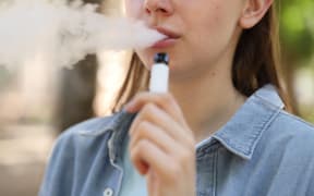 Young woman using electronic smoking device outdoors, closeup
