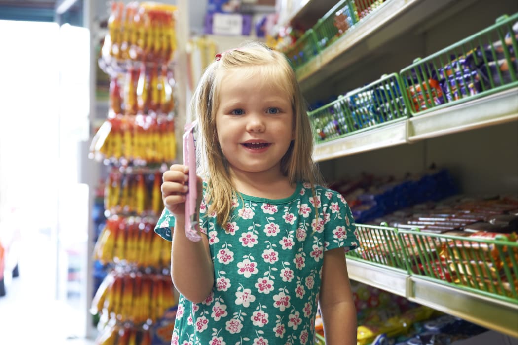 A little girl with a big smile stands next to the lolly aisle at a supermarket (file)