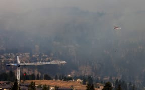 A firefighting helicopter ferries water as it battles the McDougall Creek wildfire in Kelowna, British Columbia, Canada. Wildfires bore down on Canada's Yellowknife and Kewlona on 18 August, 2023, with firefighters in the west bracing for another 'scary' night as stunned refugees from the far north began arriving at shelters after their entire city was evacuated. The blazes have caused 'terrible loss', Prime Minister Justin Trudeau told reporters after meeting evacuees from Yellowknife, capital of the Northwest Territories, as they arrived in Edmonton, Alberta.