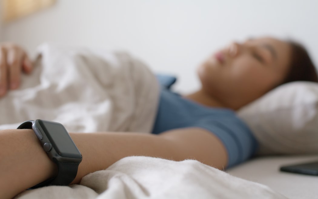Young woman sleeping while wearing smartwatch for resting sleep rate on arm.