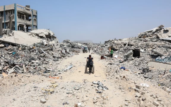 A Palestinian boy pulls a wheelchair past destroyed buildings in the al-Tuffah neighbourhood of Gaza City on August 14, 2025, following more than 22 months of war between Israel and the Palestinian militant group Hamas. The Israeli military said on August 13, that it had approved the framework for a new offensive in the Gaza Strip, as Hamas condemned what it called "aggressive" Israeli ground incursions in Gaza City. The approved plan for the expanded offensive comes days after Israel's security cabinet called for the capture of the Palestinian territory's largest city following 22 months of war that have created dire humanitarian conditions. (Photo by Omar AL-QATTAA / AFP)