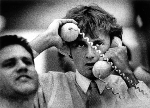A sharemarket dealer visibly distressed with a telephone held to each ear.