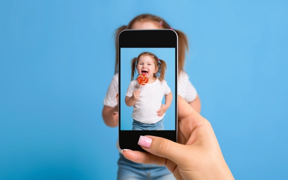 Woman's hand making photo of a little girl with a mobile phone. Selective focus on a mobile phone with a portrait of a girl. Made for social networks
