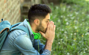 A teenage with backpack, holding his head in his hands