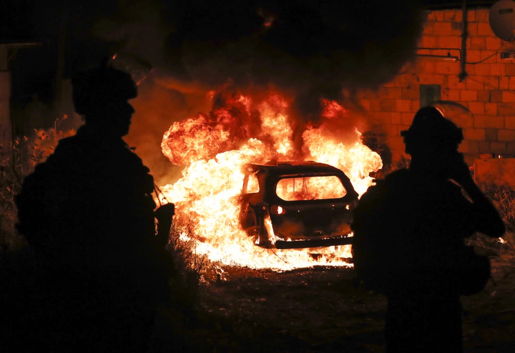 Israeli security looks on as they stand by a burning settlers car in the Sheikh Jarrah neighbourhood of Israeli-annexed east Jerusalem on May 6, 2021.