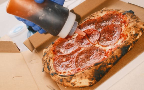 A person pouring sauce from a bottle on Bari's Pizza halal pepperoni pizza.