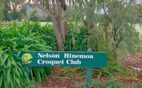 A green painted wooden sign in the carpark of the Nelson Hinemoa Croquet Club. It says "NELSON HINEMOA CROQUET CLUB"