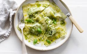 A bowl of triangular filled pasta garnished with basil leaves.