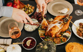 A pair of white hands carve a roast chicken on a table with other food dishes
