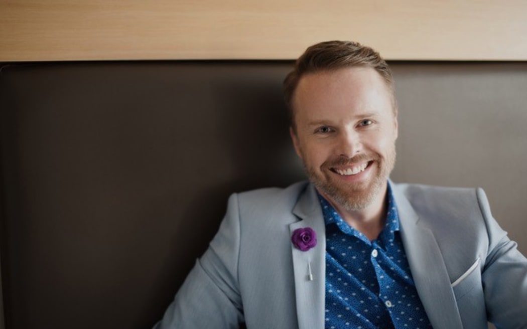 Man with beard sits on bench seat smiling