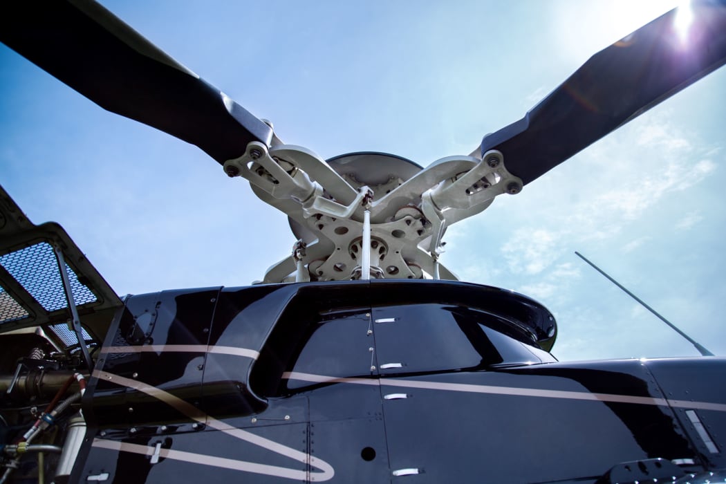 63552730 - close up of a screw of black with gray stripes bell 407 helicopter standing on green grass field in blue sky background.