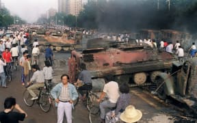 A file photo taken on 4 June, 1989 shows Beijing residents gathering around the smoking remains of over 20 armoured personnel carriers burnt by demonstrators during clashes with soldiers near Tiananmen Square.