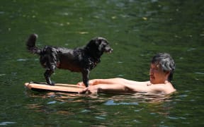 A man swims with his dog in a canal in Beijing on June 22, 2023. Swathes of northern China sweltered in 40-degree heat on June 22, weather data showed, as parts of Beijing and the nearby megacity of Tianjin recorded their highest temperatures for years. (Photo by GREG BAKER / AFP)