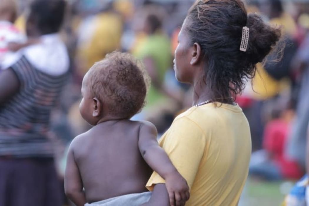 A woman nurses a child while listening intently to a campaign spiel at a political rally in Guadalcanal.
