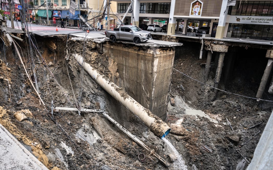 A vehicle is seen on the edge of the hole in the ground after the road collapsed near a hospital in Bangkok on September 24, 2025. A portion of a busy road in Thailand's capital caved in early on September 24, leaving a hole dozens of meters deep in front of a main hospital and forcing people nearby to evacuate. (Photo by Chanakarn Laosarakham / AFP)