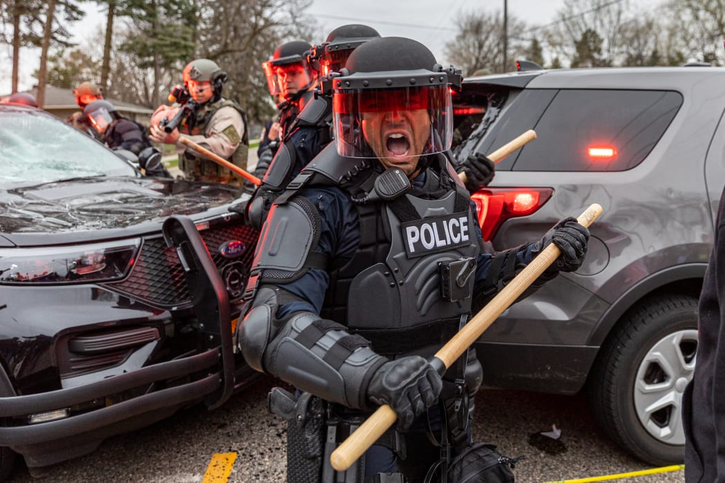 Police officers take cover as they clash with protesters after an officer shot and killed a man in Brooklyn Center, Minneapolis, Minnesota on April 11, 2021.