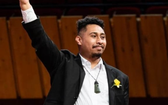 Conductor Takerei Komene smiles and his right arm is raised in the air to acknowledge the applause of the audience at the Big Sing National Finale 2022.