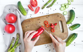 Woman hands slicing sweet pepper on wooden cutting board, surrounded by vegetables and eggs. Home cooking concept. Salad or any vegetarian dish. Flat lay, top view
