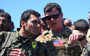a US officer, from the US-led coalition, speaking with a fighter from the Kurdish People's Protection Units (YPG) at the site of Turkish airstrikes near northeastern Syrian Kurdish town of Derik.