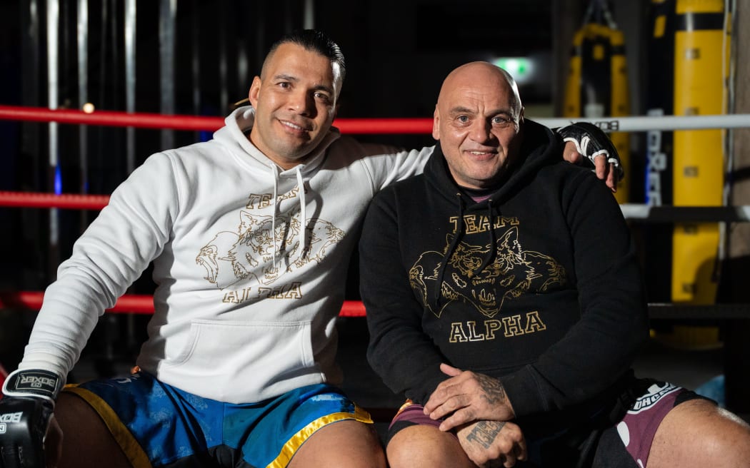 Two of the stars of the film "Kaikohe Blood & Fire" are sat on the edge of a boxing ring and looking at the camera.